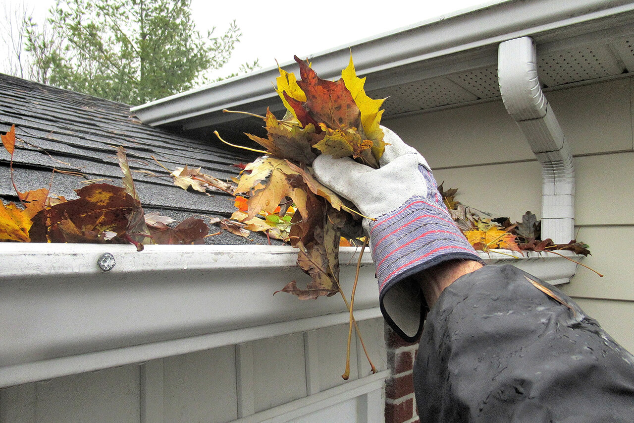 homeowner cleaning the leaves out of home gutters